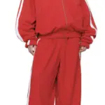 Model draagt een oversized rood trainingspak met witte biezen, bestaande uit een jack en broek, uit de LIMINALE sculpted streetwear collectie.
